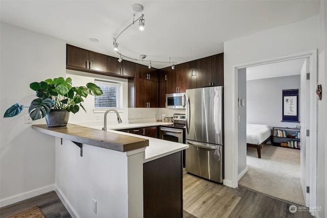 kitchen with light hardwood / wood-style floors, kitchen peninsula, stainless steel appliances, and dark brown cabinets