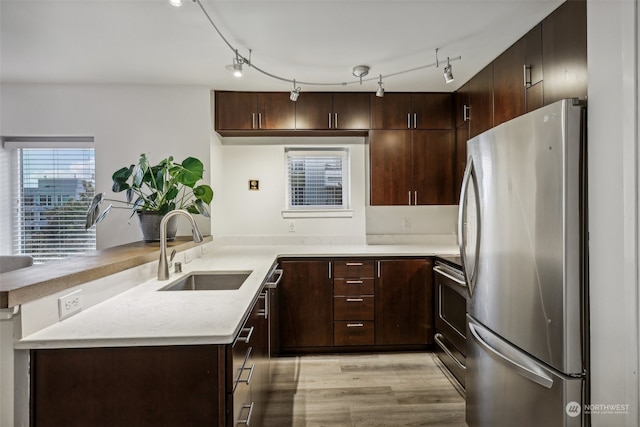 kitchen with light hardwood / wood-style flooring, kitchen peninsula, sink, dark brown cabinetry, and appliances with stainless steel finishes