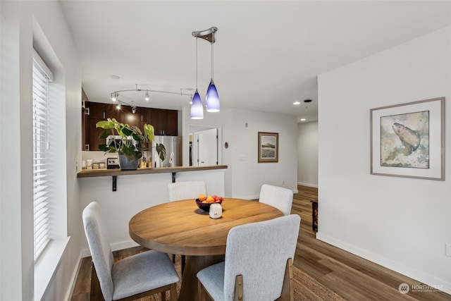 dining room with a healthy amount of sunlight, rail lighting, and dark hardwood / wood-style flooring