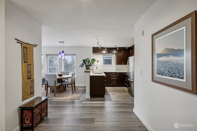 kitchen with dark hardwood / wood-style floors, hanging light fixtures, a center island with sink, stainless steel fridge, and sink