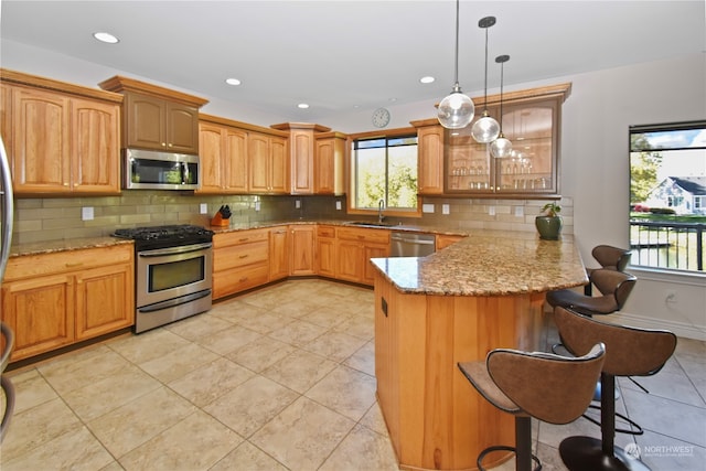 kitchen featuring appliances with stainless steel finishes, plenty of natural light, kitchen peninsula, a kitchen breakfast bar, and decorative light fixtures