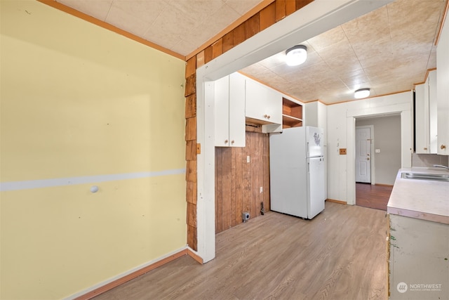 kitchen with wood walls, sink, white cabinetry, light hardwood / wood-style floors, and white fridge