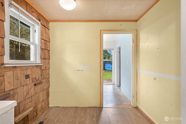 hall featuring crown molding, wood walls, and light hardwood / wood-style flooring