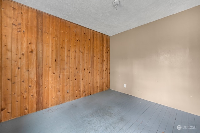 empty room with wood walls, hardwood / wood-style flooring, and a textured ceiling