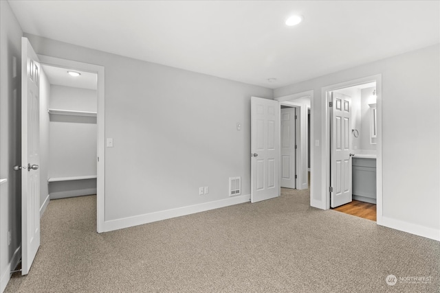 unfurnished bedroom featuring ensuite bathroom, light colored carpet, a closet, and a walk in closet