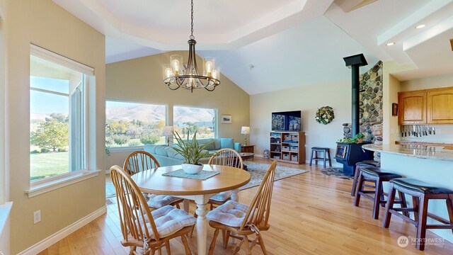 dining space featuring light hardwood / wood-style floors, a wood stove, a notable chandelier, and vaulted ceiling