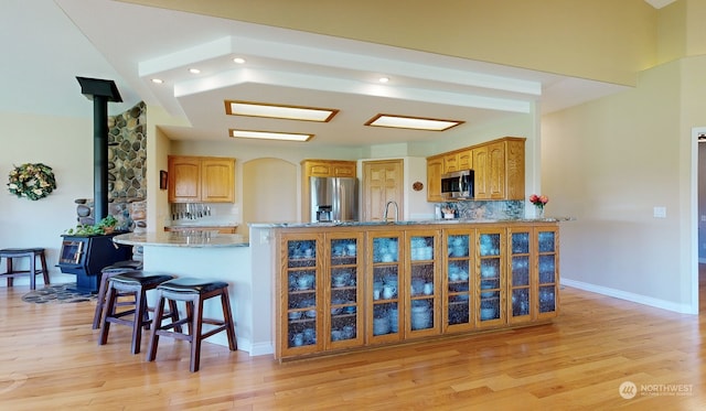 kitchen with kitchen peninsula, appliances with stainless steel finishes, light hardwood / wood-style flooring, and a wood stove