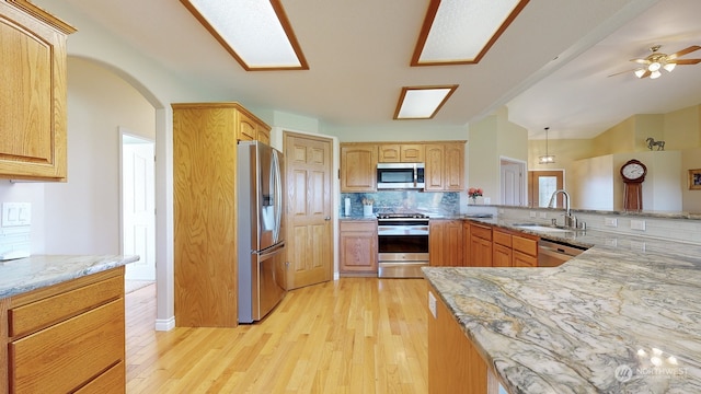 kitchen featuring kitchen peninsula, backsplash, appliances with stainless steel finishes, light hardwood / wood-style floors, and sink