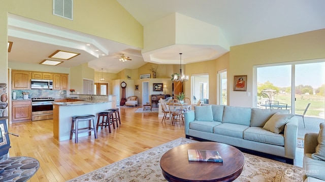 living room with high vaulted ceiling, sink, ceiling fan with notable chandelier, and light wood-type flooring