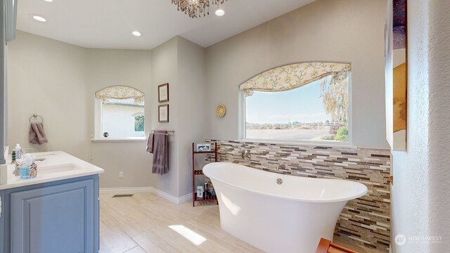 bathroom featuring a wealth of natural light, vanity, a chandelier, and a washtub