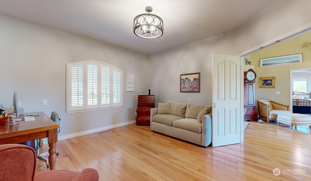 home office with light hardwood / wood-style floors and a notable chandelier