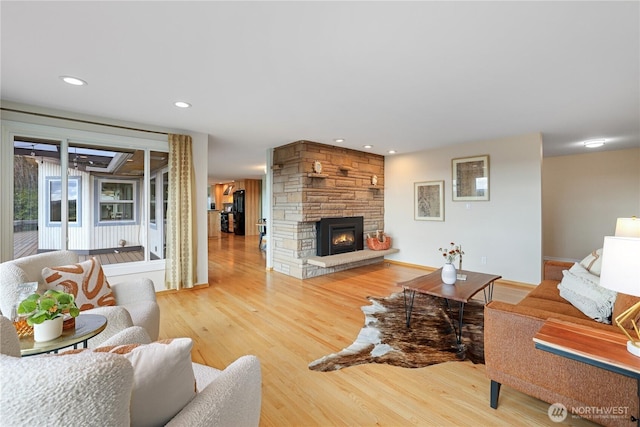 living room featuring a stone fireplace, recessed lighting, and light wood-style floors