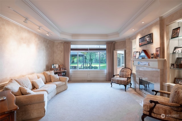 living room with a raised ceiling, a tile fireplace, ornamental molding, track lighting, and light colored carpet