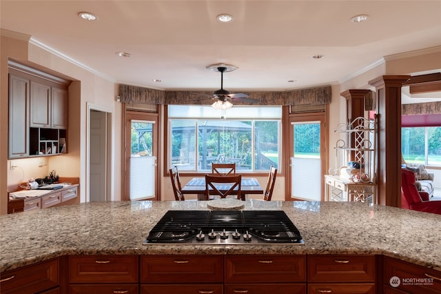 kitchen featuring stainless steel gas cooktop, ornate columns, ceiling fan, light stone counters, and ornamental molding