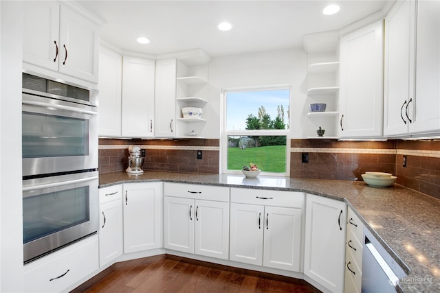 kitchen featuring white cabinets, tasteful backsplash, dark hardwood / wood-style flooring, dark stone counters, and stainless steel double oven