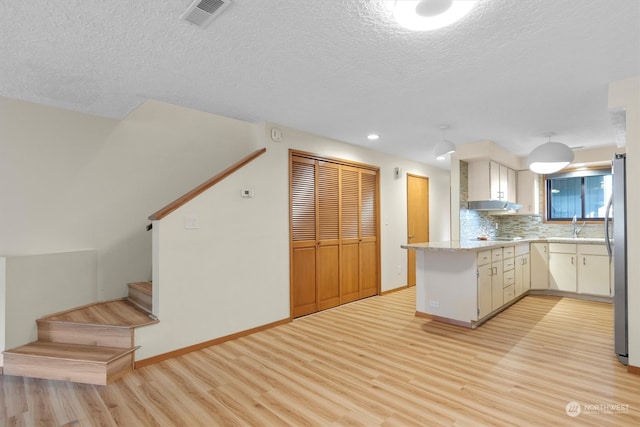 kitchen with stainless steel fridge, white cabinets, kitchen peninsula, and light wood-type flooring