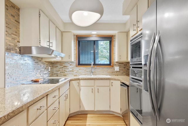 kitchen featuring light stone countertops, sink, light wood-type flooring, stainless steel appliances, and decorative backsplash