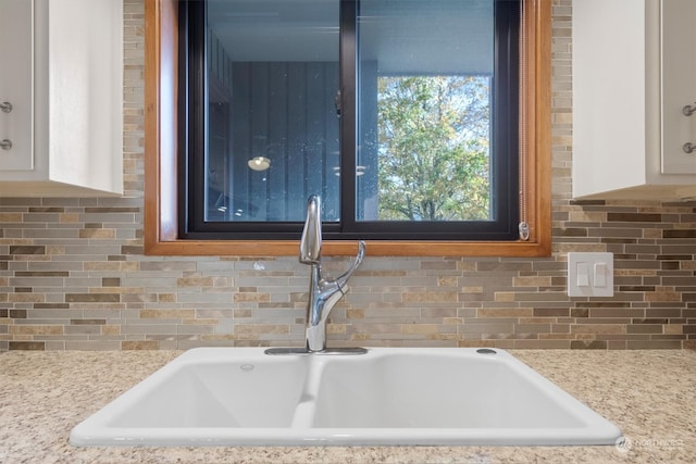 room details featuring white cabinets, light stone countertops, and sink