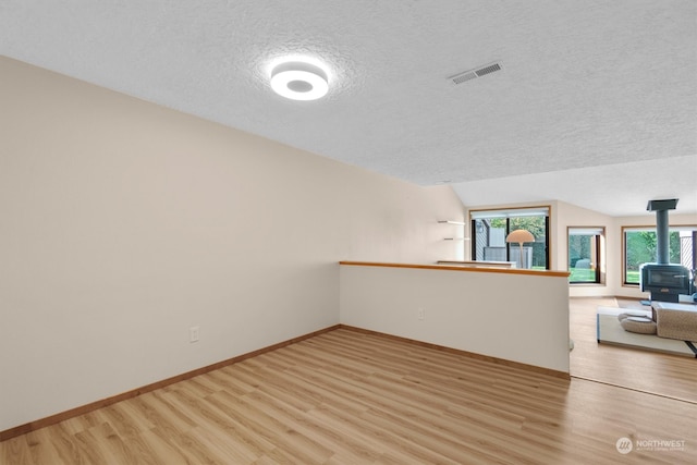 empty room with light hardwood / wood-style floors, a wood stove, a textured ceiling, and vaulted ceiling