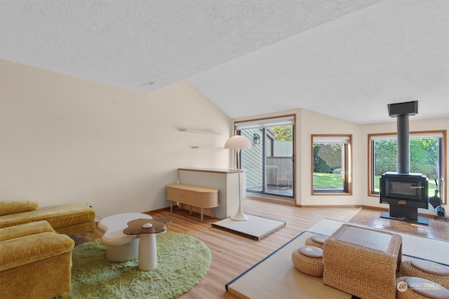 living room featuring lofted ceiling, light hardwood / wood-style flooring, a wood stove, and plenty of natural light