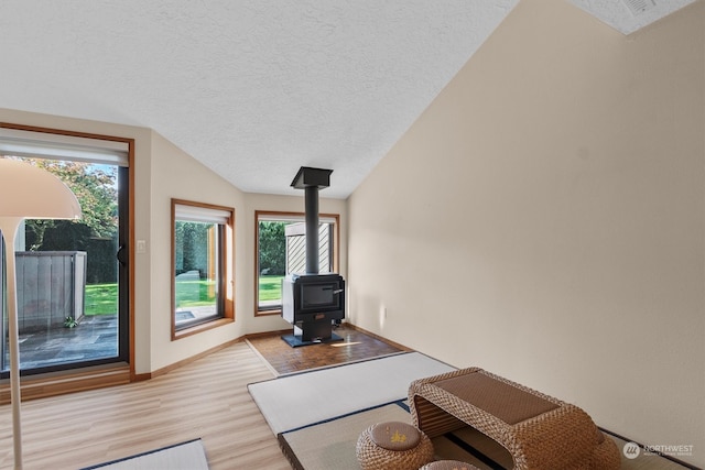 living room featuring light hardwood / wood-style floors, a wood stove, a textured ceiling, and lofted ceiling