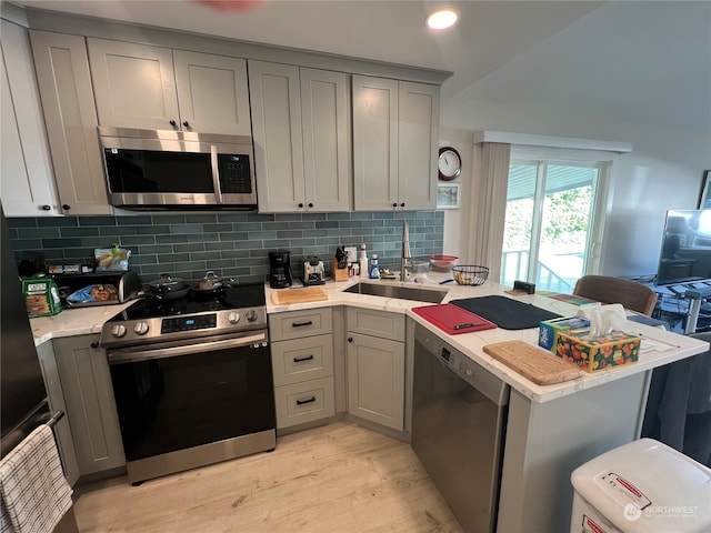 kitchen with kitchen peninsula, appliances with stainless steel finishes, light wood-type flooring, gray cabinetry, and sink