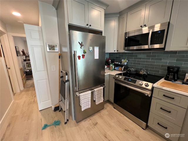 kitchen with appliances with stainless steel finishes, light hardwood / wood-style flooring, decorative backsplash, and gray cabinets