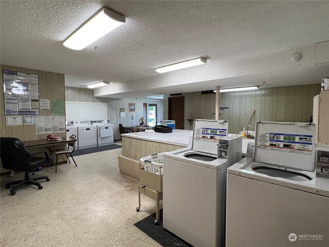 clothes washing area with a textured ceiling, wooden walls, and separate washer and dryer