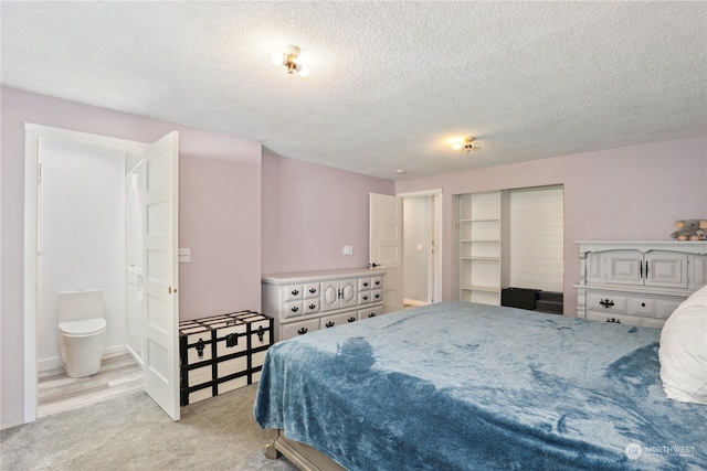 bedroom featuring a closet, light hardwood / wood-style flooring, a textured ceiling, and ensuite bath