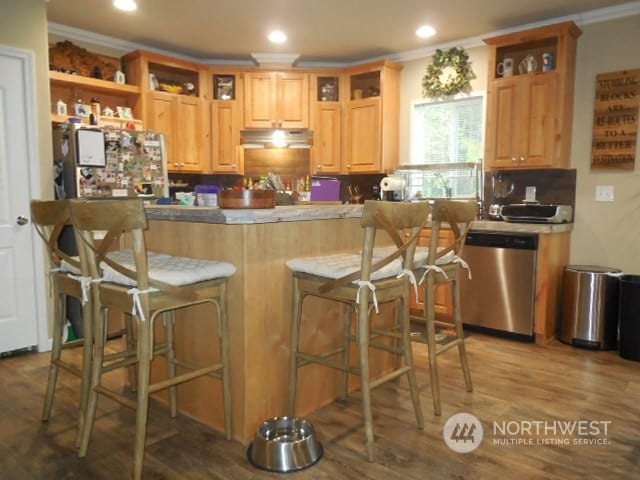 kitchen with a kitchen bar, stainless steel dishwasher, white fridge, hardwood / wood-style flooring, and ornamental molding