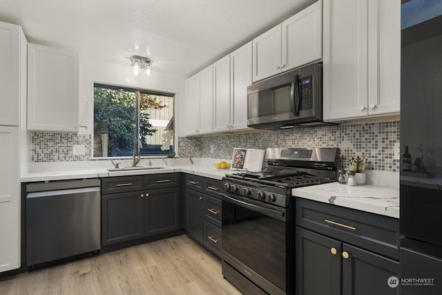 kitchen with appliances with stainless steel finishes, tasteful backsplash, sink, white cabinets, and light hardwood / wood-style flooring