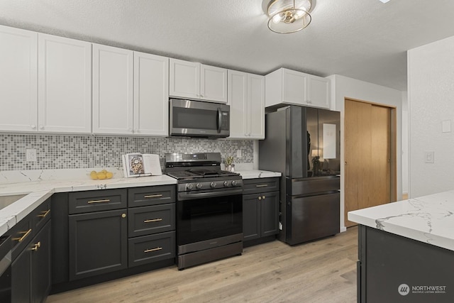 kitchen featuring white cabinetry, tasteful backsplash, light wood-type flooring, stainless steel appliances, and light stone countertops