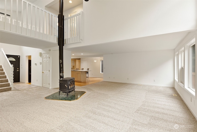 living room featuring a towering ceiling, a wood stove, and light colored carpet