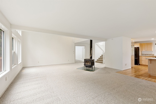 unfurnished living room featuring light colored carpet and a wood stove