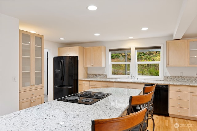 kitchen featuring a breakfast bar area, light brown cabinetry, light hardwood / wood-style flooring, black appliances, and sink