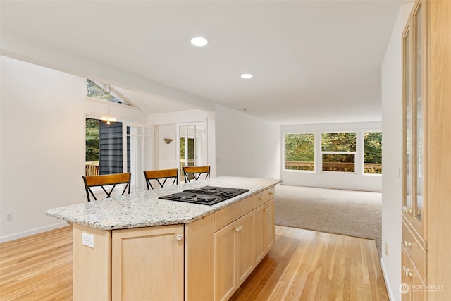 kitchen featuring a kitchen island, light brown cabinets, a kitchen breakfast bar, black cooktop, and light hardwood / wood-style floors