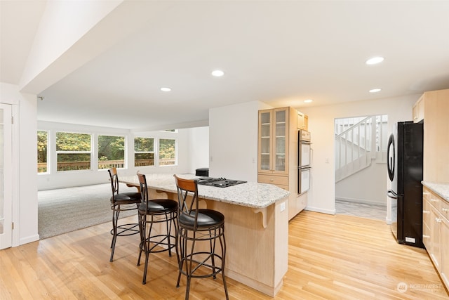 kitchen with a kitchen bar, a center island, light wood-type flooring, and refrigerator