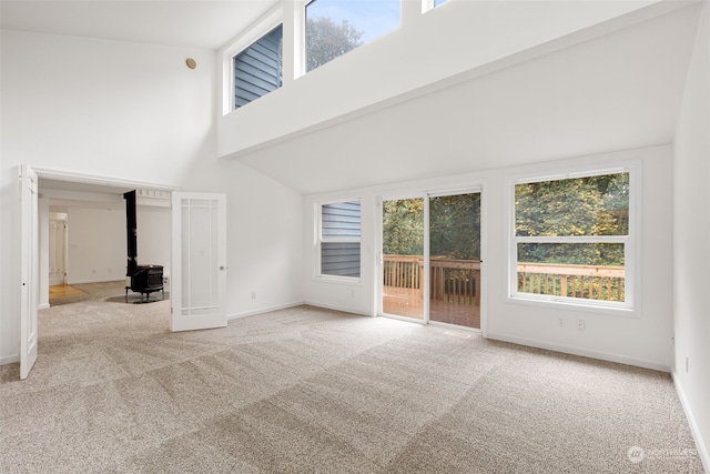 unfurnished living room with high vaulted ceiling, a wood stove, and light colored carpet