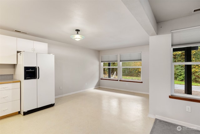 kitchen with white refrigerator with ice dispenser, plenty of natural light, and white cabinets