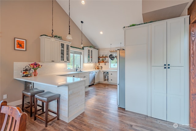 kitchen featuring kitchen peninsula, a breakfast bar, pendant lighting, white cabinets, and high vaulted ceiling