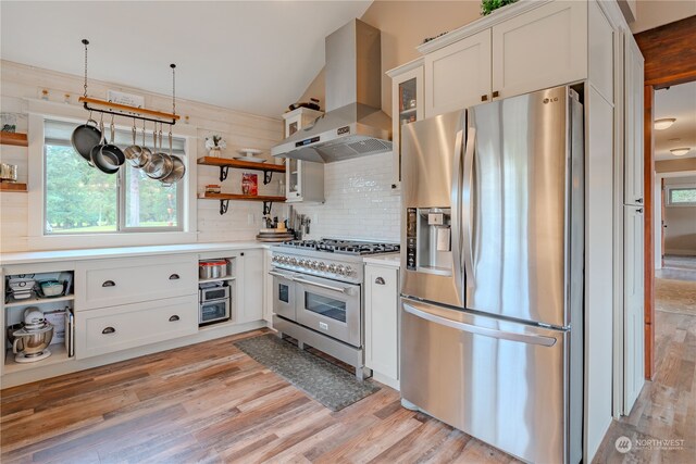 kitchen featuring white cabinetry, wall chimney exhaust hood, appliances with stainless steel finishes, and light wood-type flooring