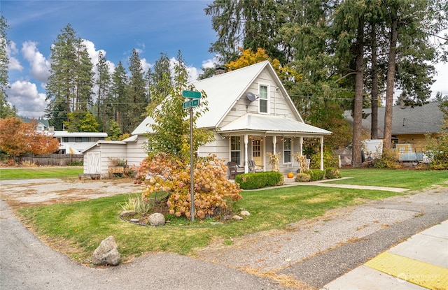 bungalow-style house with a chimney, a storage shed, covered porch, a front yard, and metal roof