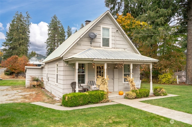 bungalow-style house featuring a porch, a front lawn, a chimney, and metal roof