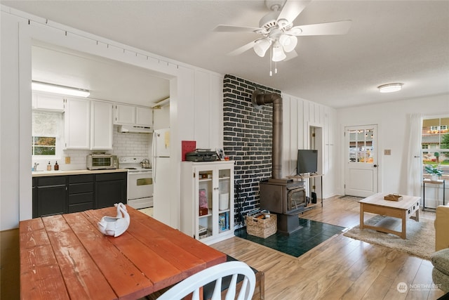 kitchen featuring white range with electric cooktop, light wood-style flooring, a wood stove, white cabinets, and under cabinet range hood