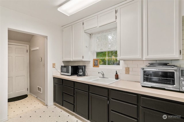 kitchen featuring white cabinets, stainless steel microwave, light countertops, light floors, and a sink