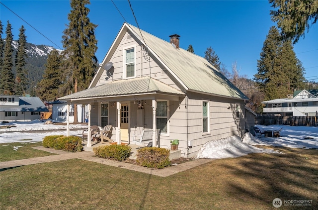 bungalow-style house with metal roof, a chimney, a front lawn, and a porch