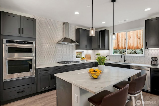 kitchen featuring a kitchen island, a breakfast bar, sink, stainless steel appliances, and wall chimney range hood