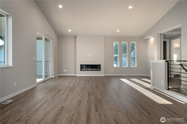 unfurnished living room featuring lofted ceiling, recessed lighting, visible vents, a glass covered fireplace, and wood finished floors