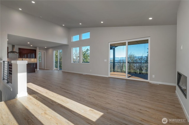 unfurnished living room with wood finished floors, a glass covered fireplace, a wealth of natural light, and recessed lighting