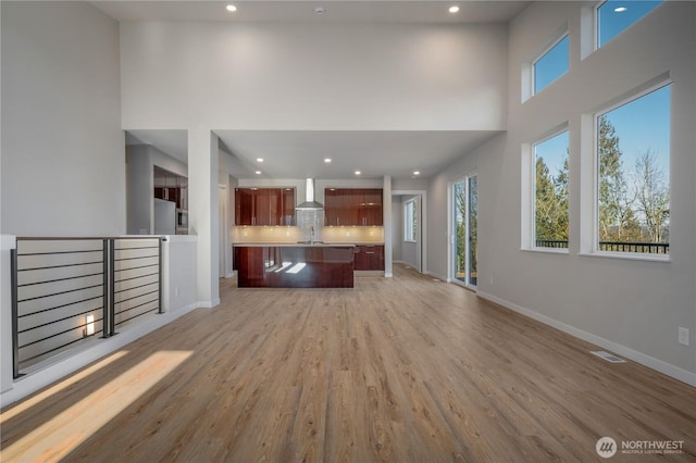 unfurnished living room featuring visible vents, baseboards, a high ceiling, light wood-style floors, and recessed lighting